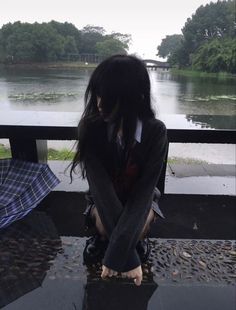 a woman sitting on top of a wet ground next to an umbrella in the rain