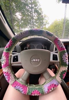 the steering wheel cover is crocheted with pink, green and purple flowers on it