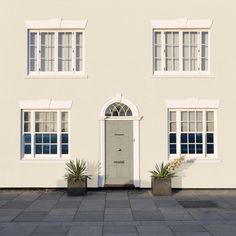 a white house with three windows and two potted plants