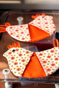 two orange birds sitting on top of a table next to a cell phone and sewing machine