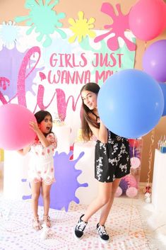 two girls standing in front of a backdrop with balloons