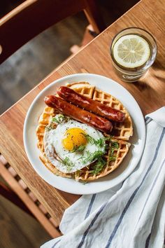 a waffle with eggs and bacon on it next to a glass of lemon juice