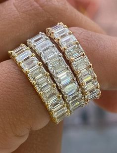 a woman's hand holding three gold rings with baguets on each band