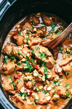 a wooden spoon in a slow cooker filled with meat and vegetables, garnished with parsley