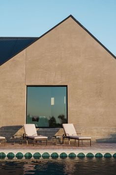 two lounge chairs sitting on the side of a swimming pool next to a large building