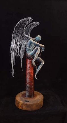 a wire sculpture sitting on top of a wooden pole with an angel in the middle