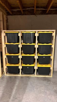 several bins are lined up in a storage room with yellow shelves and black containers