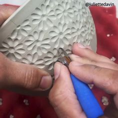 two hands are working on a sculpture with blue plastic handles and one hand is holding a small object in the other hand