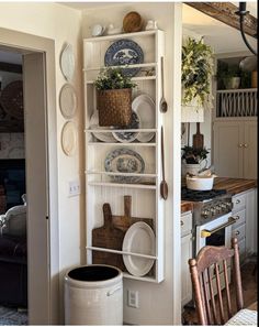 a kitchen filled with lots of dishes on top of a white book shelf next to a wooden chair