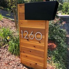 a wooden mailbox sitting on the side of a road next to a tree and bushes