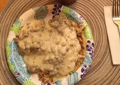 a plate topped with meat covered in gravy next to a fork and knife