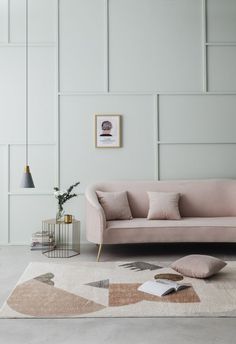 a pink couch sitting on top of a white rug next to a table and lamp