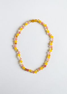 a yellow and pink beaded bracelet on a white surface with an orange tag hanging from it