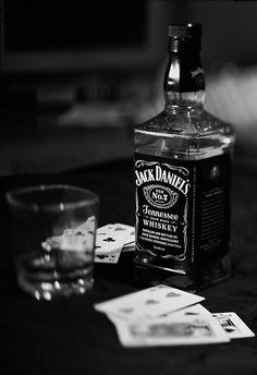 a bottle of jack daniels whiskey next to a glass and playing cards on a table