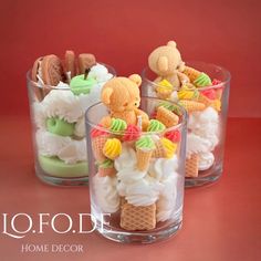 three clear cups filled with ice cream and teddy bears in the middle, sitting on a red surface