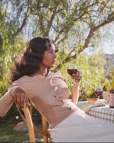 a woman sitting at a table with a glass of wine in her hand and looking off into the distance