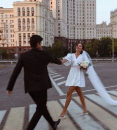 a bride and groom crossing the street in front of tall buildings with their arms around each other