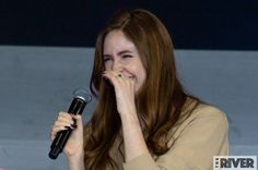 a woman with long red hair holding a microphone in her hand and smiling at the camera