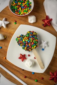 a heart shaped lollipop with sprinkles and stars on the side