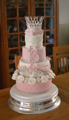 a three tiered cake with roses and a tiara on top is sitting on a table