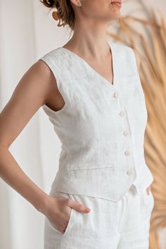 Discover effortless style with our Linen Vest Button-Up Top, a versatile addition to your wardrobe. Crafted from premium linen fabric, this top exudes casual elegance and breathability, perfect for warm weather days. Featuring imitation pockets for added detail, it offers a touch of sophistication. Pair this versatile top with our matching Linen Shorts for a coordinated look, perfect for leisurely strolls or weekend brunches. Mix and match with our Oasis linen pants in your wardrobe to create di White V-neck Vest With Pockets, White Linen Sleeveless Vest, White Linen Vest For Workwear, Summer Linen Vest With Pockets, White Linen Casual Vest, White V-neck Vest With Buttons, White Summer Workwear Vest, White Summer Vest With Pockets, Elegant White Vest With Buttons