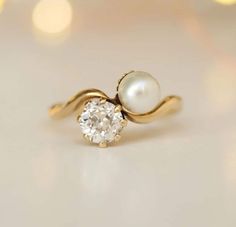 a pearl and gold ring on a white surface with lights in the backround