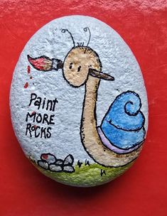 a painted rock with a bird holding a paintbrush on it's face and the words paint more rocks