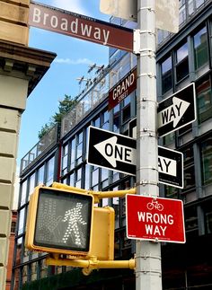 street signs on a pole in front of a building and traffic light with buildings in the background