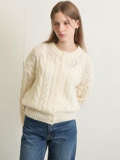 a young woman is standing in front of a white wall wearing jeans and a sweater