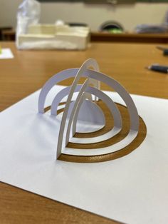 a paper sculpture sitting on top of a wooden table next to a white piece of paper