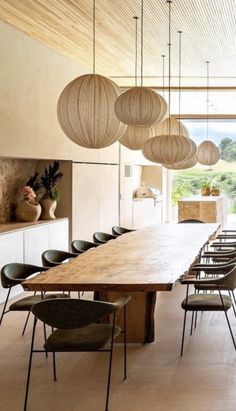 a large wooden table surrounded by chairs and hanging light fixtures in a room with white walls