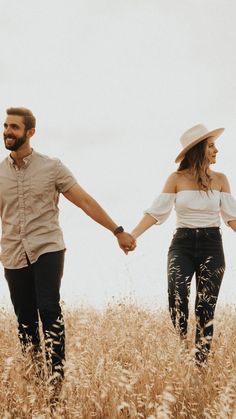 a man and woman holding hands walking through tall grass