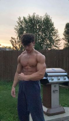 a shirtless man standing in front of a bbq with his hands on his hips