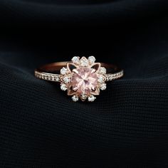 a pink diamond ring on top of a black cloth with white diamonds around the band