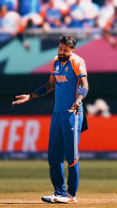 a man standing on top of a field wearing blue and orange pants with his hands out