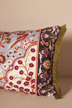 a decorative pillow with tassels and flowers on the front is sitting on a beige surface