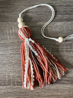 an orange and white tasseled necklace on a wooden surface with beads hanging from it