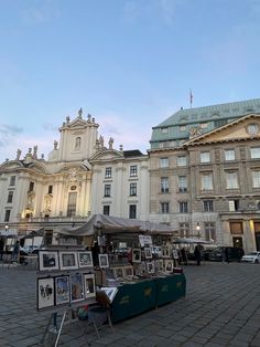 an outdoor market in front of a large building with many pictures on the tables and umbrellas