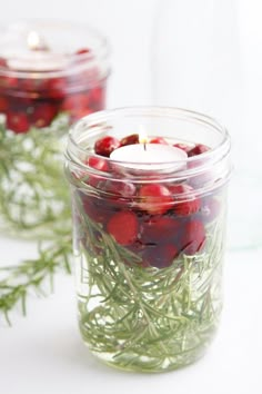 two jars filled with cranberries and greenery