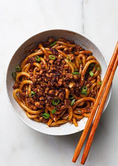 a bowl filled with noodles and meat next to chopsticks on a white surface