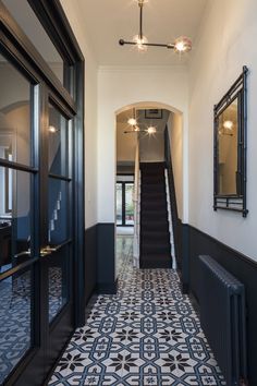 a hallway with black and white tile flooring next to a stair case in a home