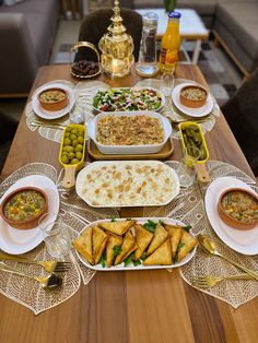 a table filled with lots of food on top of plates next to bowls and spoons