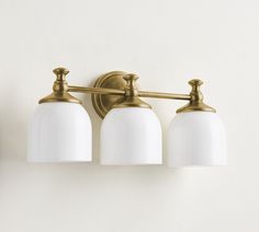 three light bathroom fixture with white glass shades and brass finish, on a white wall