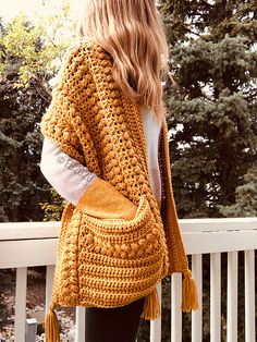 a woman wearing a yellow crochet purse standing on a porch