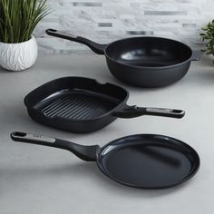 three black frying pans sitting on top of a counter next to a potted plant