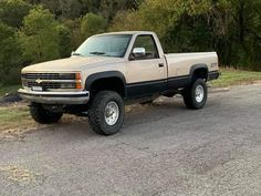 a beige truck parked on the side of a road in front of some grass and trees