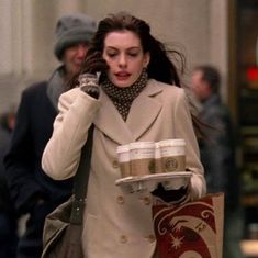 a woman is walking down the street talking on her cell phone and carrying coffee cups