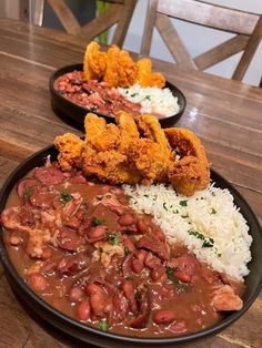 two plates filled with rice, beans and fried chicken on top of a wooden table