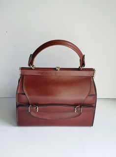 An early Essell vintage leather bag, made in France, dating from the 1930's. A stunning and very useable brown leather bag. The leather is nice and thick and good quality. It has a lift up clasp  opening which reveals one main compartment which is lined with a cream ribbed taffeta fabric and has one zipped side pocket and two small slip pockets for tickets etc.  The bag has a brass plated frame and clasp and to the front of the bag a front flap which sits in a belt like strap and underneath there is a slip pocket.  Measurements Height: 16.5cm Width: 20cm Depth: 10cm at base ( tapered) Handle length: 22cm Condition: Externally the bag is in excellent vintage condition, the leather is beautiful and looks fantastic for its age. Internally the lining is quite marked with a lot of signs of use Thirties Fashion, Art Deco Bag, Brown Leather Clutch, Tooled Leather Bag, Womens Bag, Taffeta Fabric, Small Leather Bag, Vintage Leather Bag, Brown Leather Bag