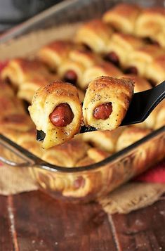 two hotdogs are being held in a casserole dish with a spoon